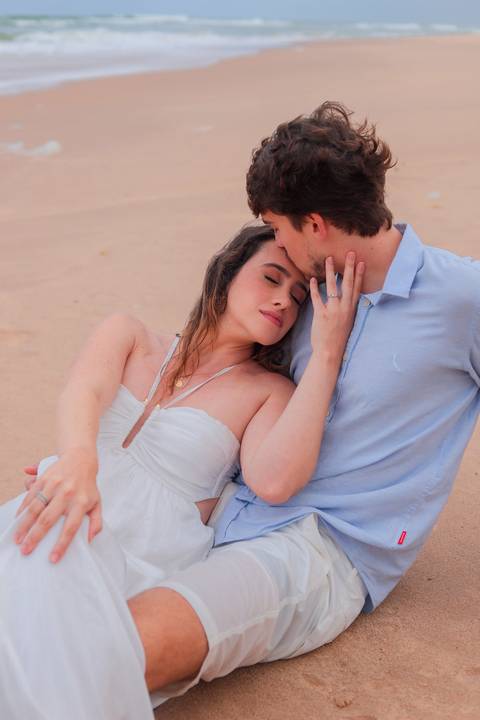Noivos rolando na areia, rindo e vivendo o momento. Um ensaio que mostra que o verdadeiro amor também se diverte.'