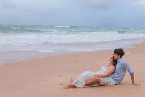 Noivos rolando na areia, rindo e vivendo o momento. Um ensaio que mostra que o verdadeiro amor também se diverte.'