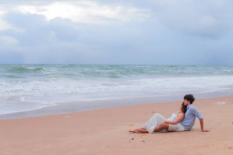 Noivos rolando na areia, rindo e vivendo o momento. Um ensaio que mostra que o verdadeiro amor também se diverte.'