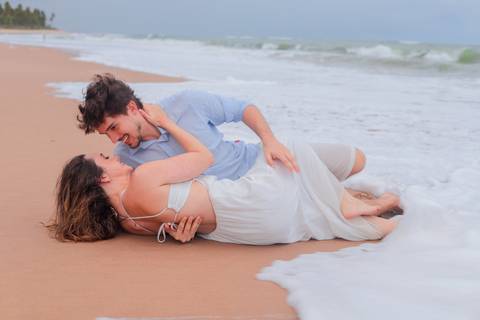 Noivos rolando na areia, rindo e vivendo o momento. Um ensaio que mostra que o verdadeiro amor também se diverte.'