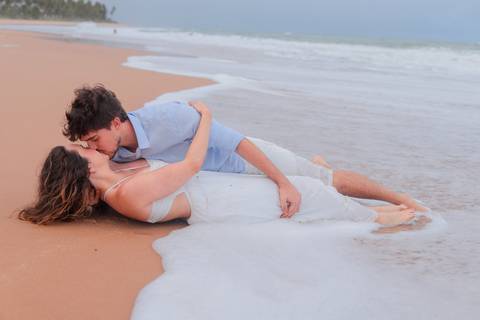 Noivos rolando na areia, rindo e vivendo o momento. Um ensaio que mostra que o verdadeiro amor também se diverte.'