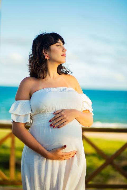 Maria Paula grávida, sorrindo ao lado de Bruno, em momento de afeto registrado por Waldyr Lantyer, fotógrafo especializado em ensaios gestantes em Praia do Forte Bahia e áreas como o Iberostar.'