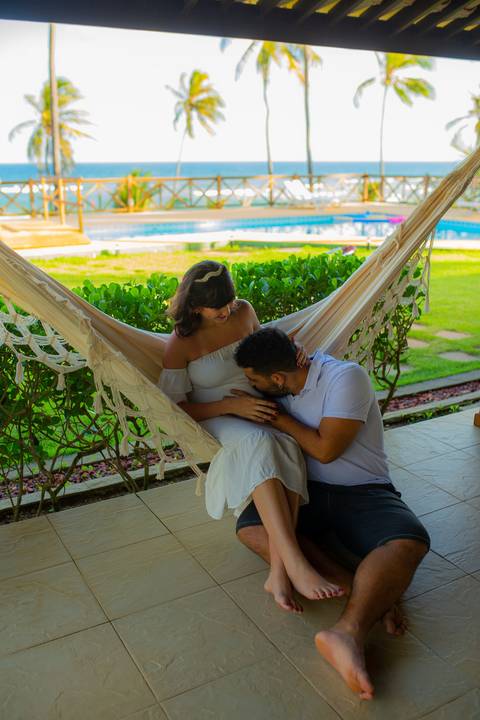 Gestante de branco deitada na rede com o marido em casa de praia em Barra do Jacuípe, próximo ao Iberostar, em ensaio realizado por Waldyr Lantyer, fotógrafo na Praia do Forte Bahia.'