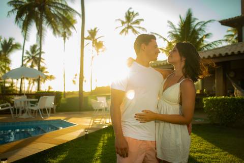Toque simbólico na barriga da gestante com pôr do sol ao fundo, no deck de madeira em Barra do Jacuípe, fotografado por Waldyr Lantyer, fotógrafo de famílias na região da Praia do Forte Bahia e Iberostar.'