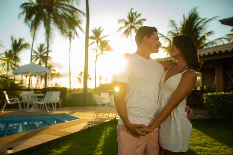 Toque simbólico na barriga da gestante com pôr do sol ao fundo, no deck de madeira em Barra do Jacuípe, fotografado por Waldyr Lantyer, fotógrafo de famílias na região da Praia do Forte Bahia e Iberostar.'