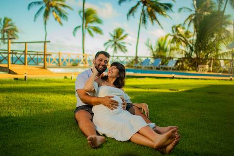 Gestante de branco deitada na rede com o marido em casa de praia em Barra do Jacuípe, próximo ao Iberostar, em ensaio realizado por Waldyr Lantyer, fotógrafo na Praia do Forte Bahia.'