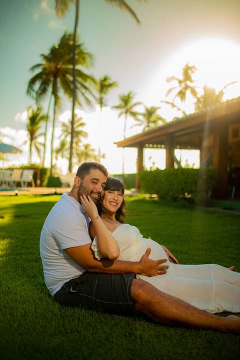 Gestante de branco deitada na rede com o marido em casa de praia em Barra do Jacuípe, próximo ao Iberostar, em ensaio realizado por Waldyr Lantyer, fotógrafo na Praia do Forte Bahia.'