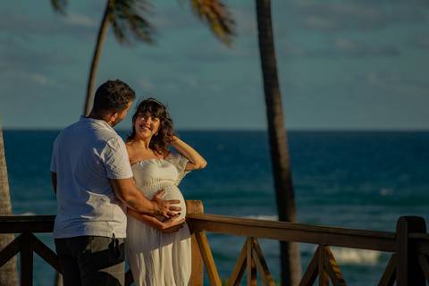 Casal mineiro trocando carinho na rede em varanda com vista para o mar, em ensaio gestacional produzido por Waldyr Lantyer, fotógrafo especializado na Praia do Forte Bahia e região do Iberostar.'