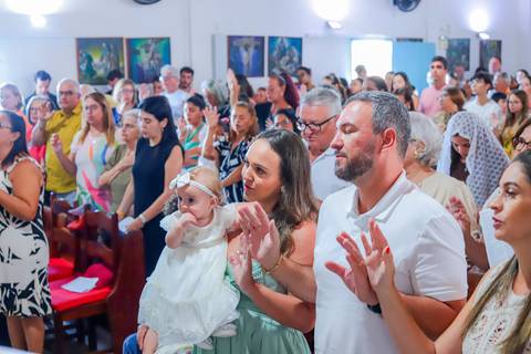 Pais emocionados segurando a bebê Catarina durante o batizado em Praia do Forte, com cenário encantador e luz suave da manhã.'