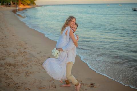 O que fazer em Praia do Forte Bahia, Fotógrafo em PRAIA DO FORTE BAHIA, WALDYR LANTYER.  Casal recém-casado celebrando elopement wedding na Praia do Forte com o céu colorido do crepúsculo ao fundo.'