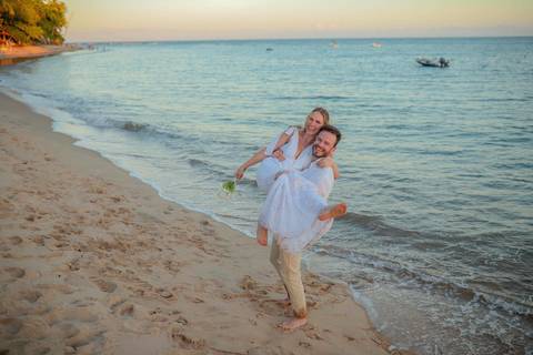 O que fazer em Praia do Forte Bahia, Fotógrafo em PRAIA DO FORTE BAHIA, WALDYR LANTYER.  Casal recém-casado celebrando elopement wedding na Praia do Forte com o céu colorido do crepúsculo ao fundo.'