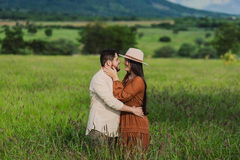 Casal se abraçando durante o ensaio pré-casamento em um campo cercado pela natureza.'