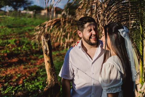 Jaque e Mateus juntos sob a sombra de uma palmeira durante ensaio de casal na zona rural.'