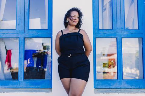 Neide durante ensaio feminino em Caetité, Bahia, fotografada em frente a uma fachada com janelas azuis.'