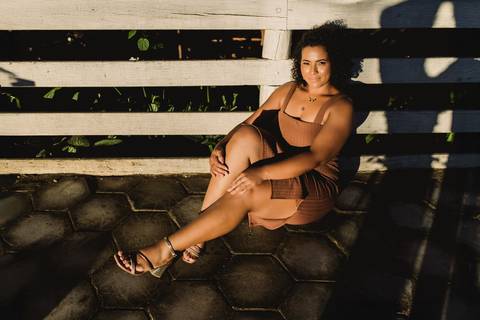 Neide sentada em um banco durante ensaio feminino, com luz e sombras criando uma composição mais marcante.'