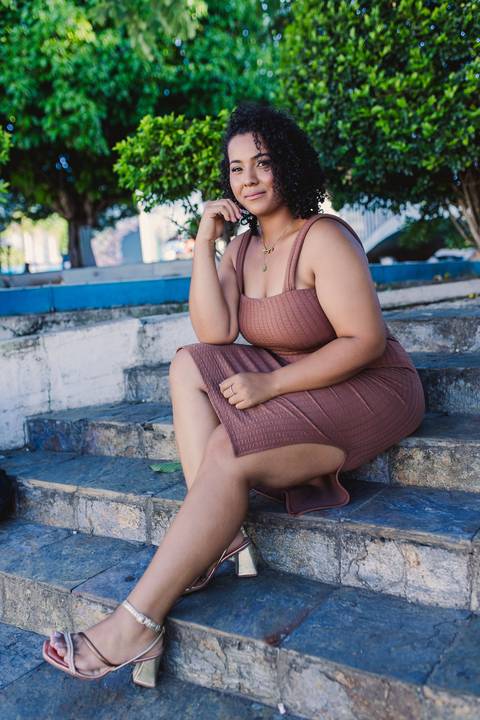 Neide sentada em uma escadaria durante seu ensaio fotográfico feminino em ambiente externo.'