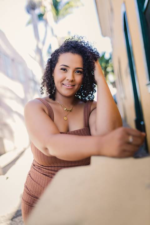 Retrato feminino de Neide sorrindo, utilizando uma fachada da cidade como parte da composição.'