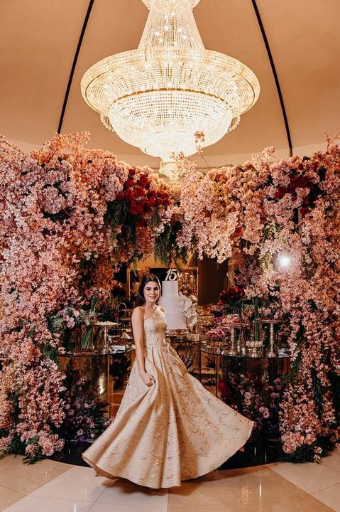 Foto da debutante em frente a mesa florida de doces'