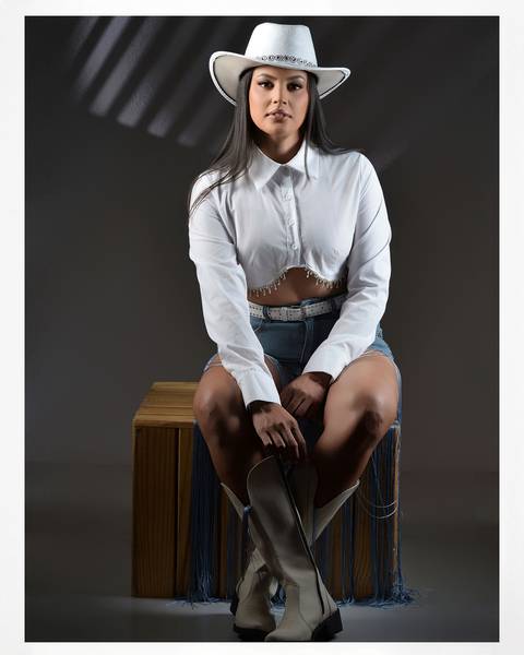 Ensaio feminino com chapéu preto e look country em estúdio fotográfico.'