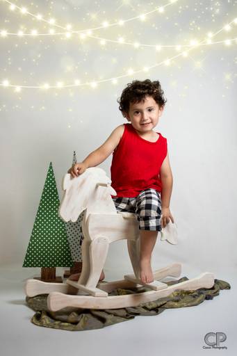 sesion de fotos navideñas en estudio fotografico en rosario con niño en caballo blanco de madera, sesiones familiares, fotografos en rosario