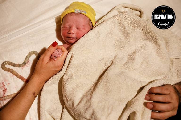 Foto de Adriana Costa de um bebê ainda ligado à placenta sendo acarinhado pelas mãos dos pais em um parto domiciliar foi premiada pela Inspiration Family Awards 