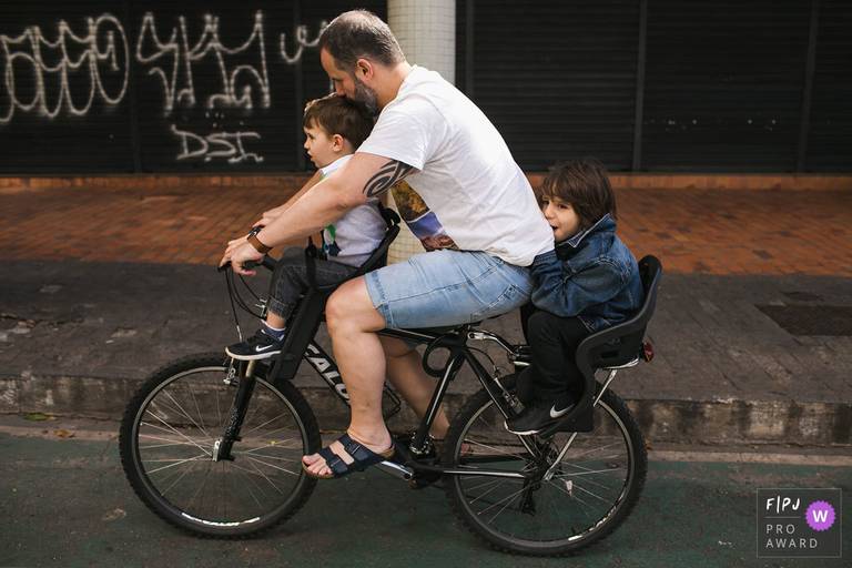 Foto de Adriana Costa, do pai e os seus dois filhos andando na mesma bicicleta, premiada internacionalmente pela Associação FPJA (Family Photojournalist Association)