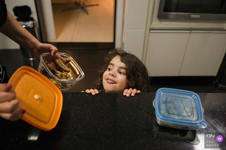 Foto de Adriana Costa premiada internacionalmente pela Associação FPJA (Family Photojournalist Association) da criança pedindo comida na cozinha para a mãe 