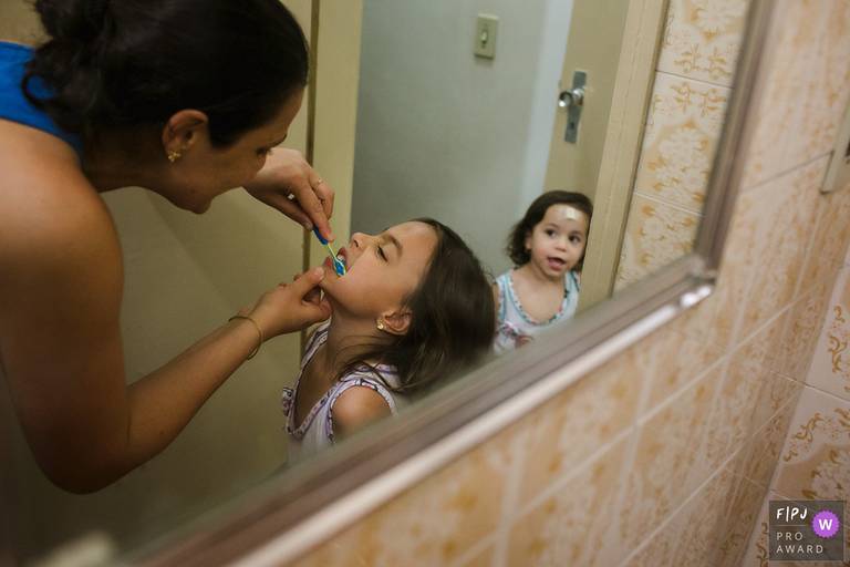 Foto de Adriana Costa da mãe escovando os dentes das filhas,  premiada internacionalmente pela Associação FPJA (Family Photojournalist Association)