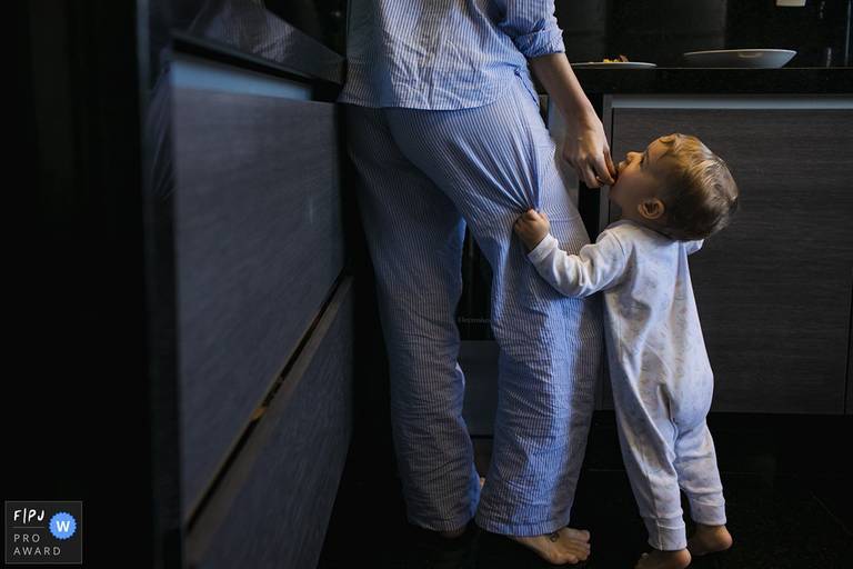 Foto de Adriana Costa premiada internacionalmente pela Associação FPJA (Family Photojournalist Association) da mãe de pijama dando um pedaço de bolo para o seu bebê na cozinha