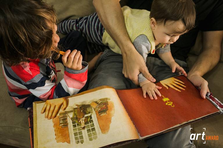 foto premiada de Adriana Costa pela fineart association de um pai e os seus dois filhos se divertindo e interagindo com um livro no momento de leitura