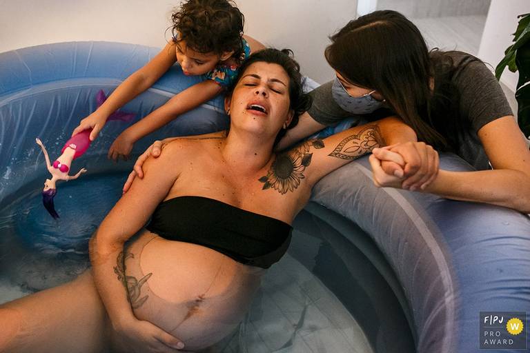 Adriana Costa foi premiada pela Associação FPJA pela foto de um parto domiciliar no qual a filha mais velha brinca com uma sereia na banheira em que sua mãe está em trabalho de parto