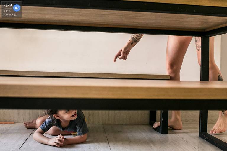 Foto de Adriana Costa de uma mãe chamando a atenção de sua filha que está debaixo da mesa foi premiada pela Associação FPJA