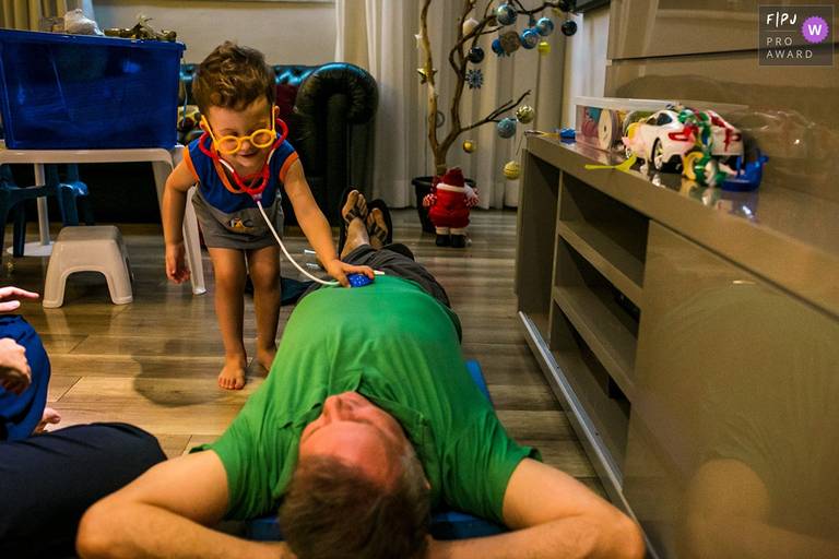 Foto de Adriana Costa de um menino brincando de examinar o pai como médico foi premiada pela Associação FPJA