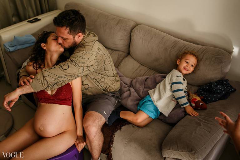 Foto de Adriana Costa sobre uma família no dia do parto do segundo filho selecionada para a galeria da Vogue Itália com o casal se beijando e seu primogênito brincando perto
