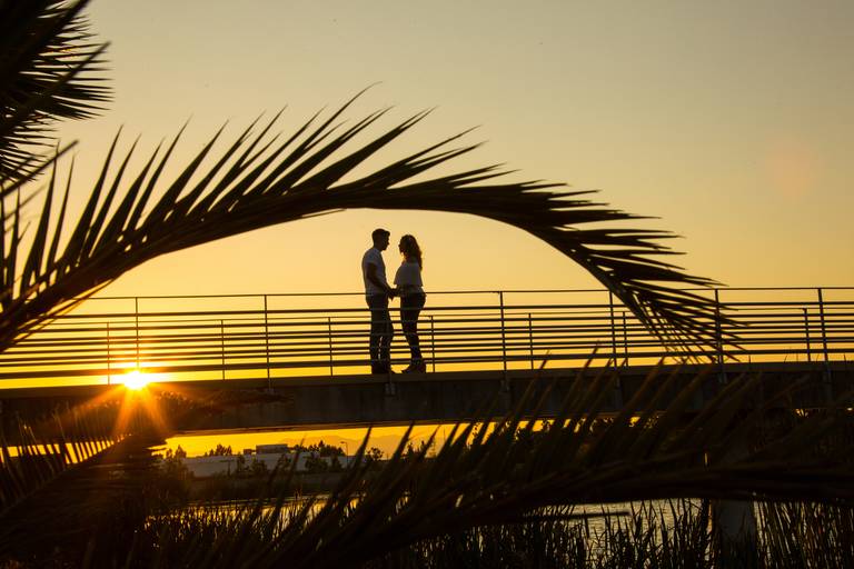 casal de namorados em cima de ponte com raios de sol passando através da estrutura da ponte