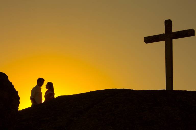 silhueta de namorados recortada na linha do horizonte com cruzeiro do seu lado direito