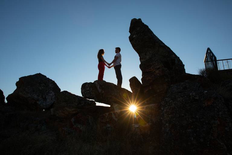 casal de namorados em cima de dois penedo com raios de sol visíveis através de brecha entre duas rochas