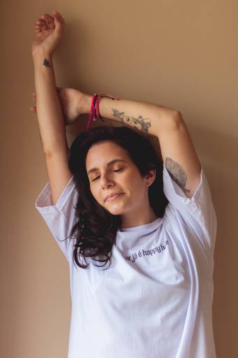 foto de mulher de olhos fechados com os braços pra cima e camiseta branca em ensaio de fotos em Florianópolis