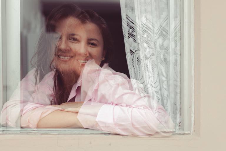 foto com sobreposição de mulher de camisa rosa apoiada na janela de casa em Florianópolis