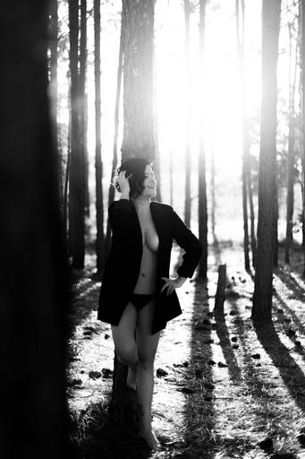 foto em preto e branco de mulher com blazer sorrindo no nascer do sol no meio de árvores no parque