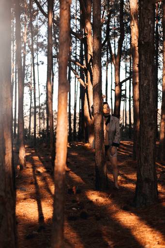 mulher de olhos fechados, de blazer encostada na árvore em parque 