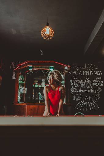 foto de mulher de body vermelho em ba, apoiada em uma mesa de sinuca