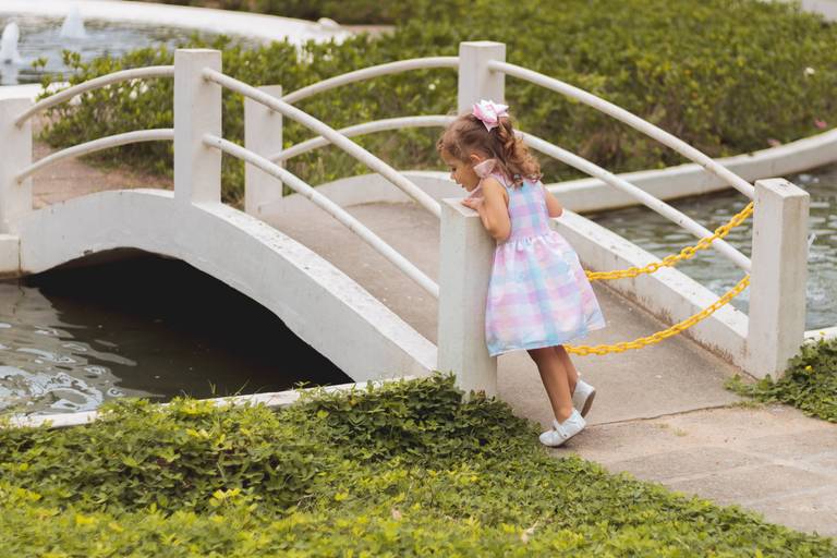 imagem de menina de vestido apoiada na ponte olhando o lago