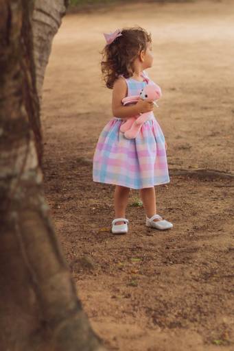 menina no parque de vestido segurando urso de pelucia rosa