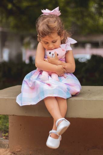 foto de criança sentada no banco do parque abraçada em seu urso de pelúcia