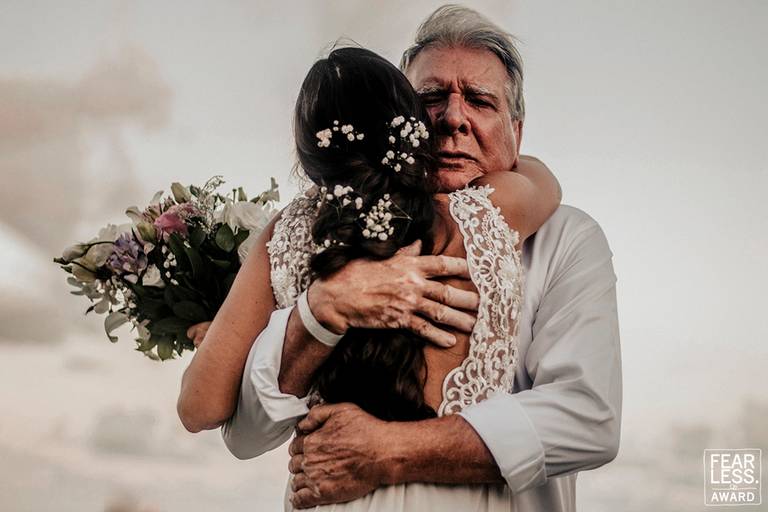 Casamento na praia, noiva com buque na mão abraçando o pai