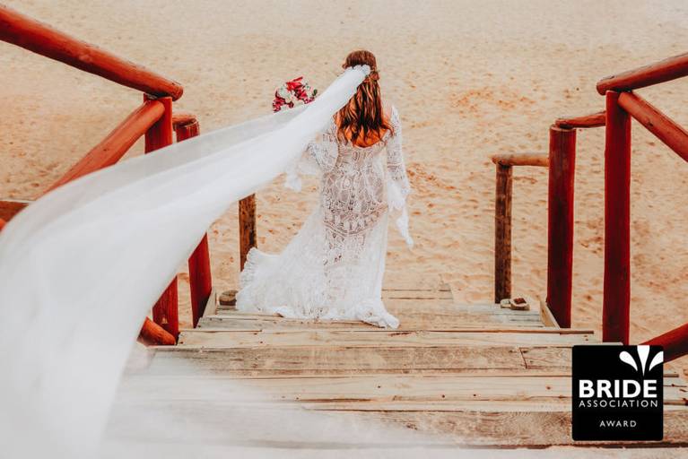 Noiva na praia, com pé na areia, buque nas mãos e véu voando na sessão de pós casamento. Casamento na Praia