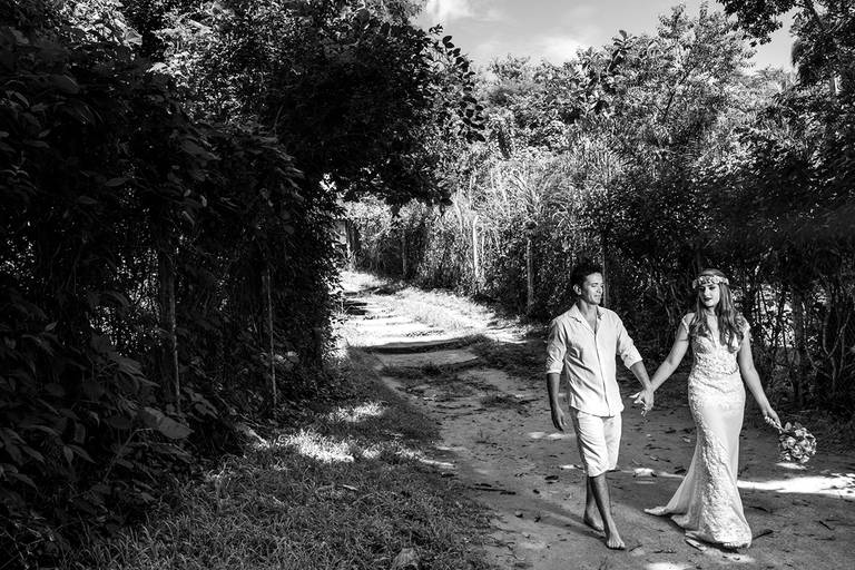 fotografia em preto e branco dos Noivos caminhando felizes de mãos dadas em chão de areia e vegetação ao fundo, Ilha grande, angra dos reis, RJ