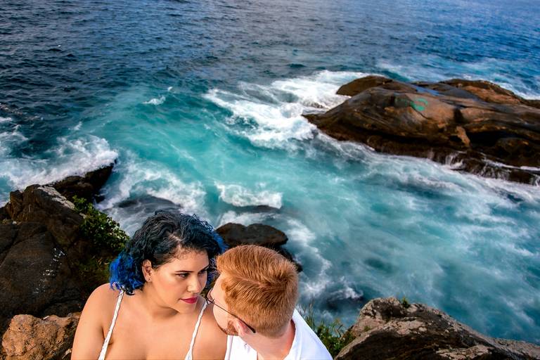 Noivos sentados na pedra da praia do forte com o lindo mar azul ao fundo se olhando apaixonadamente, Cabo Frio, Rio de Janeiro, RJ