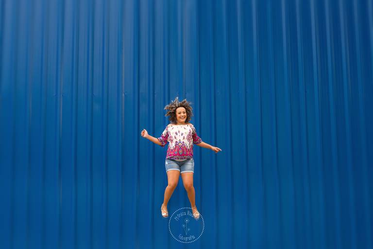 Jaque pulando em frente a uma parede de metal, toda azul, e a logo da Mônica Rivaroli Fotografia no meio da imagem